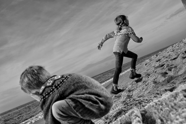 Zwei Kinder spielen am Strand auf Westerland auf der Insel Sylt. Ein kleiner Junge baggert in den sand und seine ältere Schwester rennt gerade weg