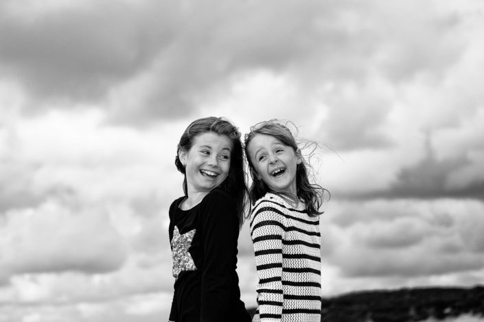 Zwei Mädchen posieren für den Fotografen vor der morsumer Wattlandschaft auf der Insel Sylt. Sie stehen Rücken am Rücken und lächeln herzlich